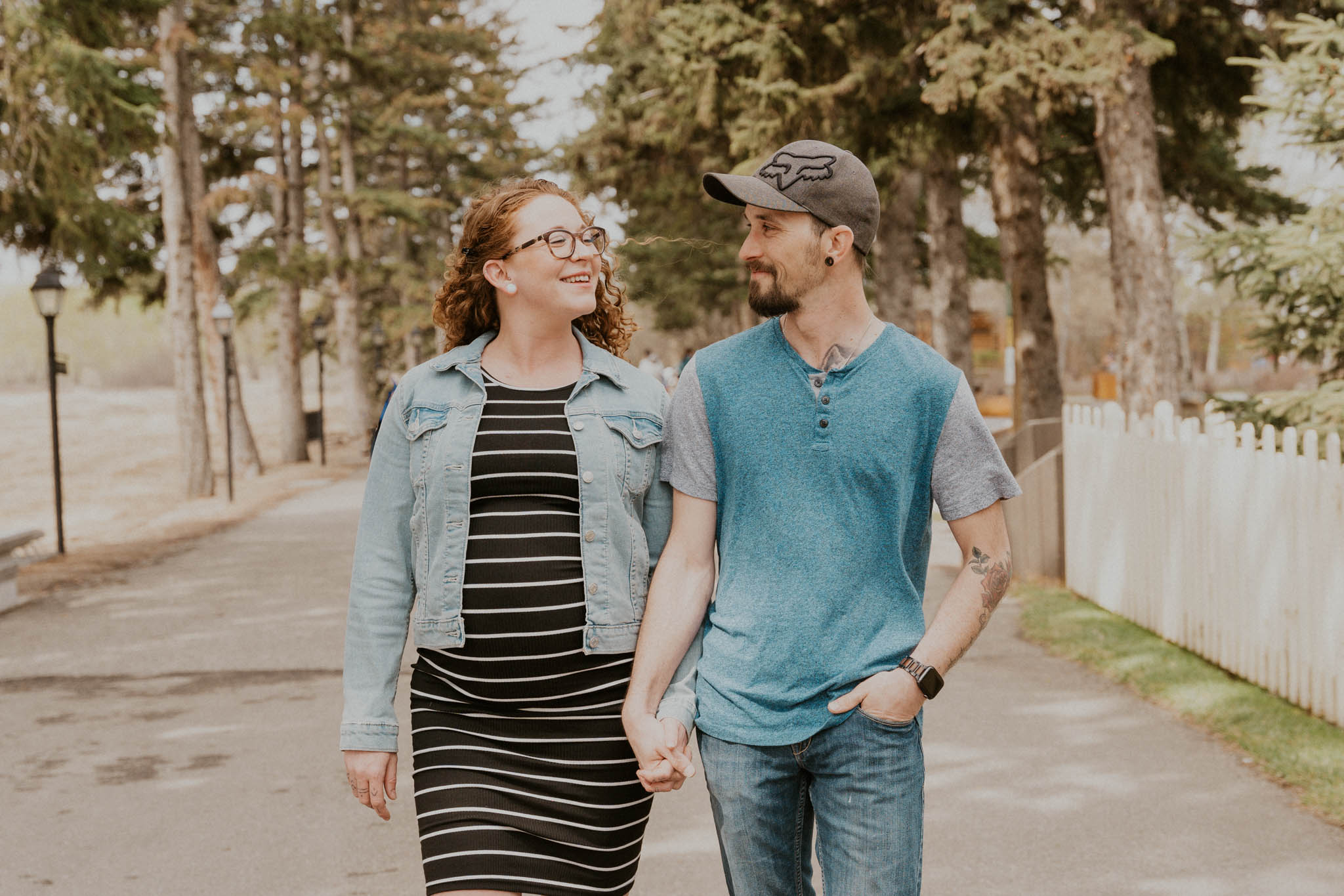 A couple walks down Fish Creek Park in Calgary holding hands for their maternity session. 